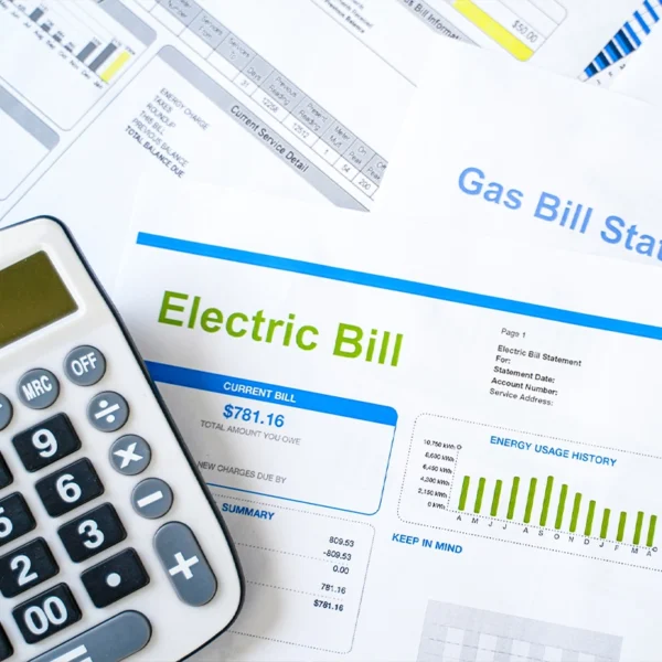 Stack of papers that contain electric and gas bills with a calculator to the left of the stack.