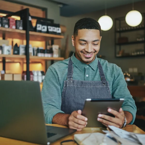 A business owner standing behind his service counter doing paperwork on his laptop and iPad.