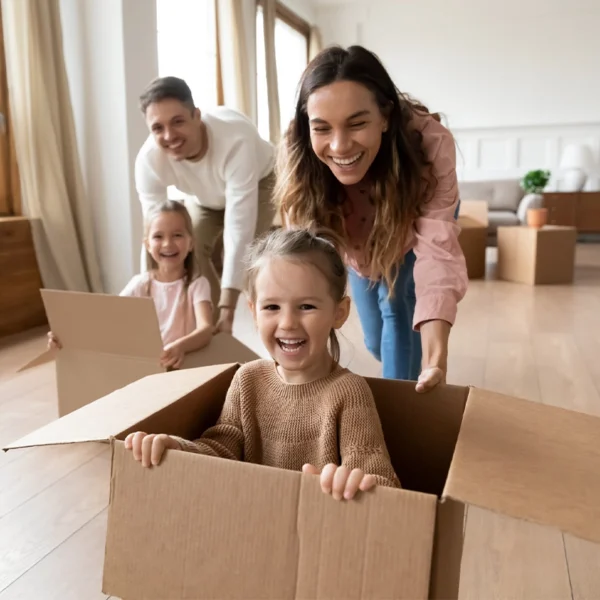 A mom and dad with their two daughters having fun moving boxes into a new home.