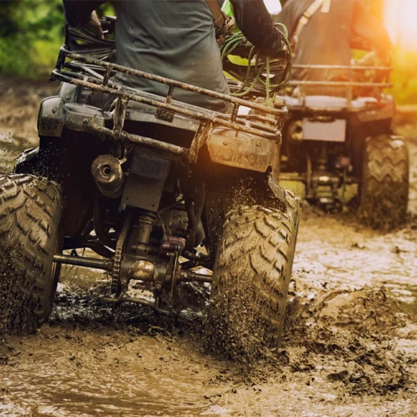Two friends riding their four-wheelers through the mud.