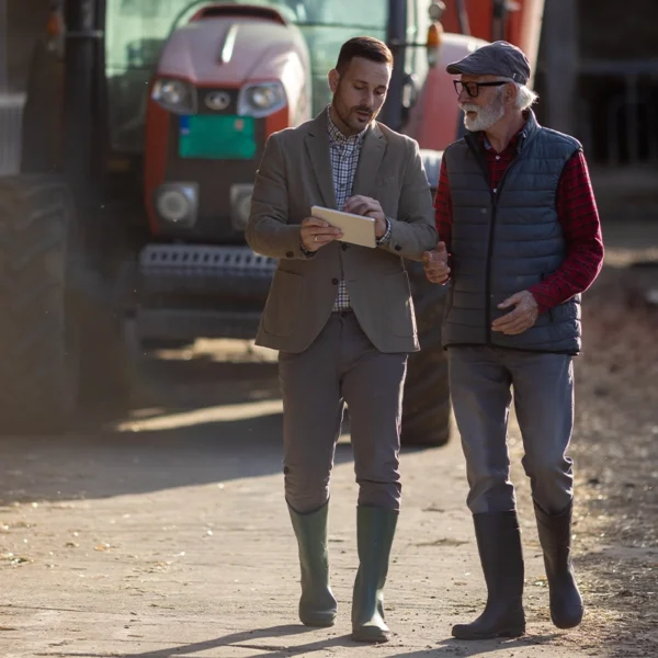 Agricultural lender meeting with a farmer near farm equipment.